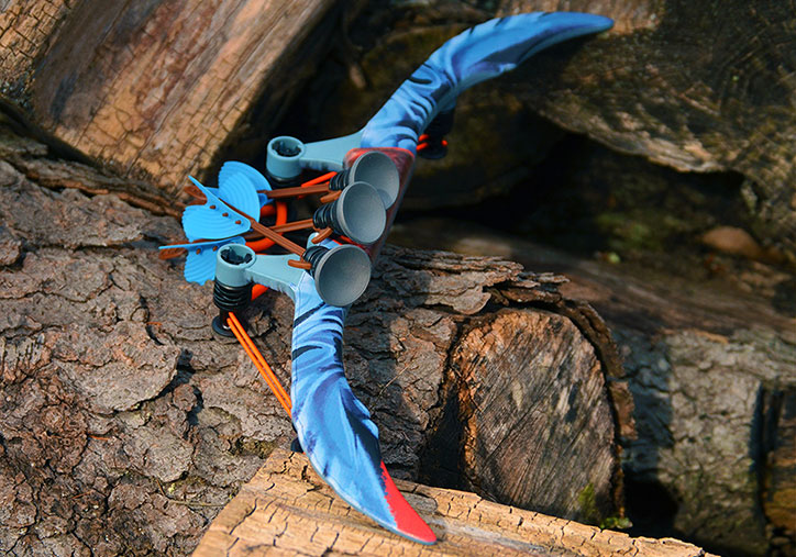 A ZING Avatar Defender Bow with 3 darts attached laid on a log