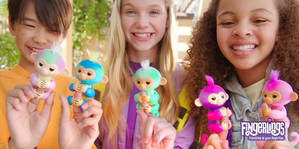 Three kids stand together with 5 Fingerlings perched on their fingers