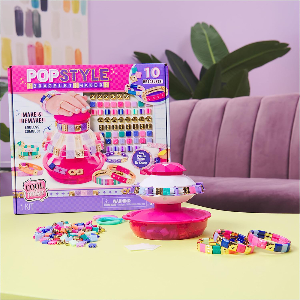 A Pop Style Bracelet Maker sits on a coffee table in a colorful living room, surrounded by the product box and assorted beads, gems, and bracelet elastic