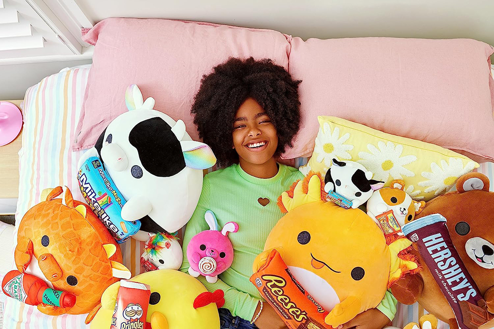 Teen girl laying down in a bed covered in both small and large Snackles plush