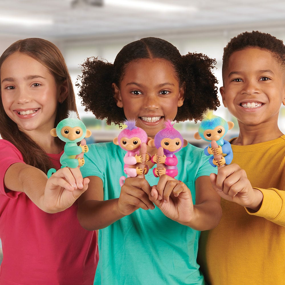 Three kids stand together with their arms stretched out, showing off all four Fingerlings characters