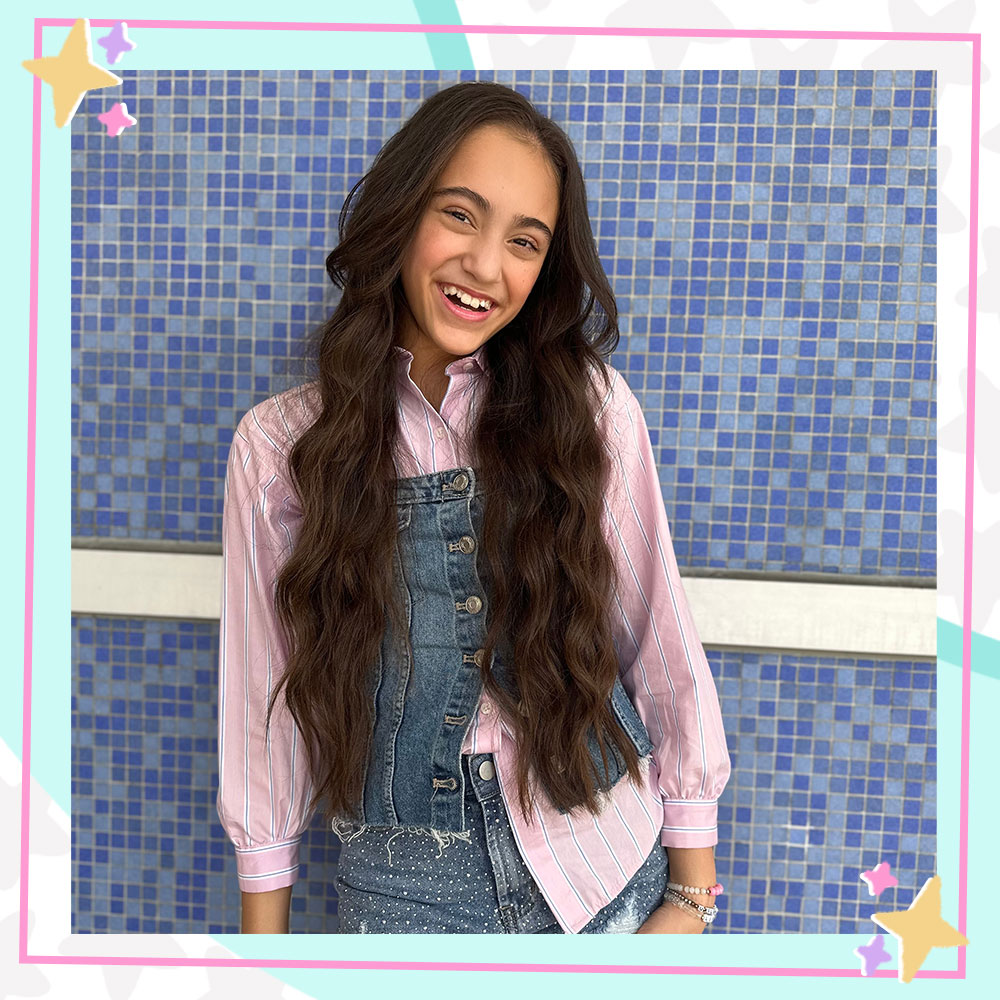 Bella Cianni in a pink striped button down shirt and denim vest smiling in front of a blue mosaic wall
