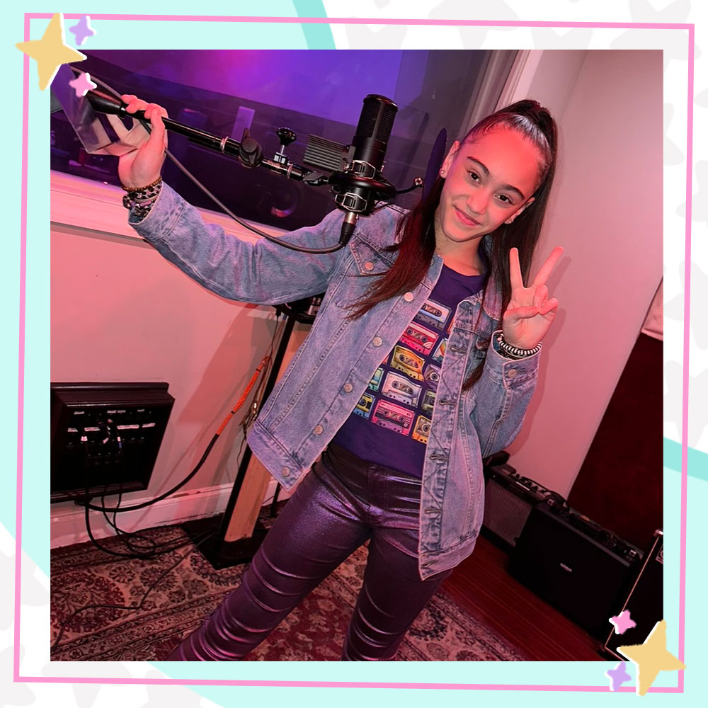 Bella Cianni holding up a peace sign while standing in front of a mic in a recording booth