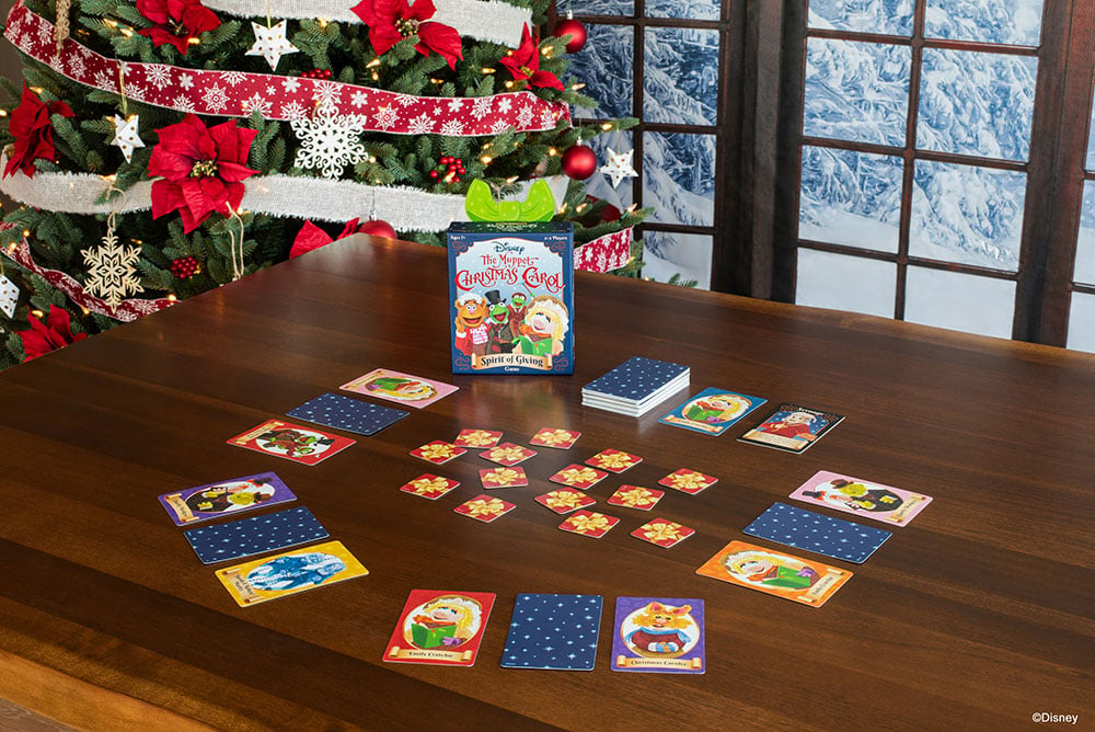The Muppets Christmas Carol Spirit of Giving Game laid out on a table in front of decorated Christmas Tree